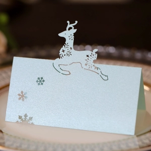 Close-up of laser-cut light blue pearlescent paper place card with reindeer and snowflake