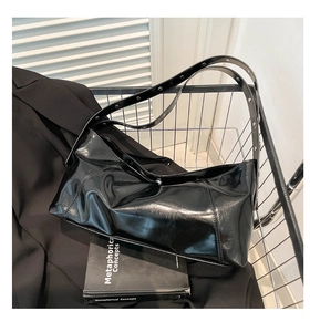 Close-up of glossy black shoulder bag with silver eyelets and adjustable strap detail