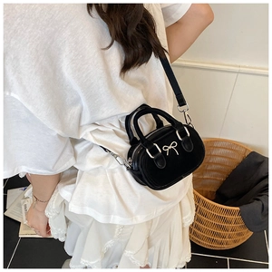 Mini black bow bowling bag shown cross-body on a model with a detachable strap