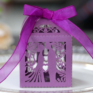 Detail of purple laser-cut wedding favor box with ribbon on white plate