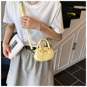 Mini yellow crossbody bowling bag with silver bow buckle worn by model in home setting