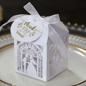 Laser-cut white wedding favor box with ribbon and Thank You tag on a gold-rimmed plate