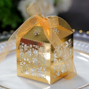 Detailed view of a golden hollow snowflake favor box with an orange chiffon ribbon