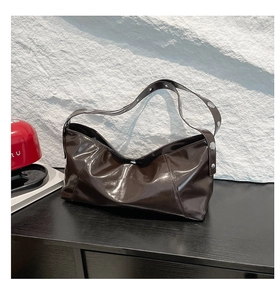 Detail of dark brown patent leather shoulder bag with silver rivet studs on black wood