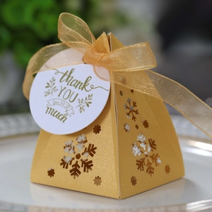 Detail van gouden piramide geschenkdoos met uitgesneden sneeuwvlok en gouden lint strik