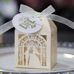 Close-up of laser-cut bride and groom wedding candy box with beige silk ribbon