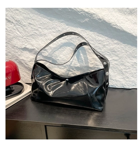 Detail of black glossy pleated shoulder bag with silver studs on stone background