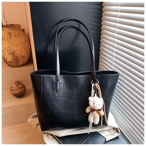 Detail of black faux crocodile tote bag with a white plush bear charm in a lifestyle setting
