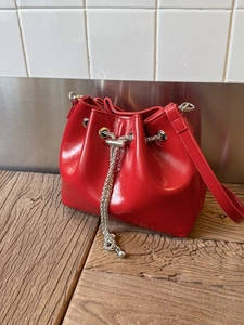 Sac seau rouge brillant avec cordon métallique posé sur une table en bois