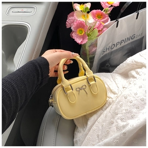 Close-up of mini yellow bowling bag with silver bow accent and top handles in car setting