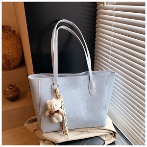 Detail of light blue crocodile texture tote bag with plush bear charm and ribbon