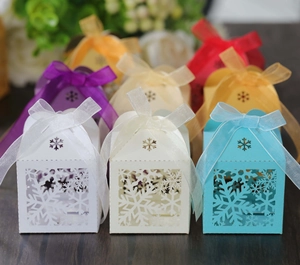 Array of colorful laser-cut snowflake gift boxes with elegant ribbon bows on dark wood