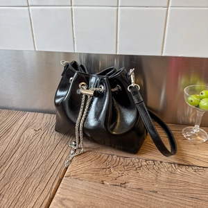 Detail shot of black glossy bucket bag with silver chain and sleek leather strap on wood