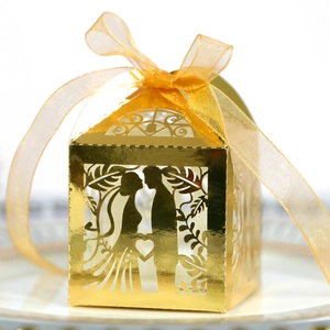 Detail of gold laser-cut wedding candy box with couple silhouette and satin ribbon