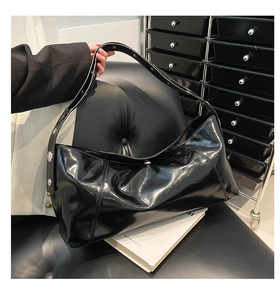 Detail view of shiny black hobo bag with silver rivets on the shoulder strap