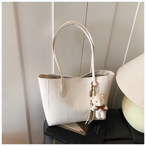 Detail of cream tote bag featuring crocodile embossing and cute teddy bear charm