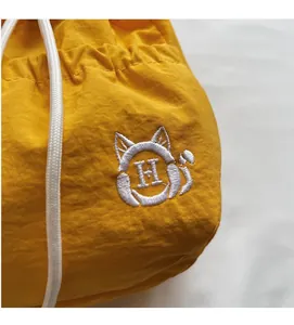 Detail of yellow nylon drawstring bag with cat ear embroidery and white H-letter logo
