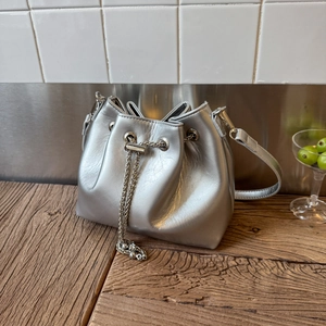 Detail of silver metallic leather bucket bag with chain drawstring on wooden surface