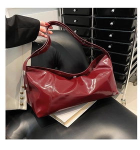 Detail of burgundy glossy faux leather hobo bag with silver buckle and wide strap