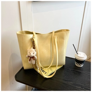 Detail of cream-colored tote bag with crocodile texture and plush bear charm