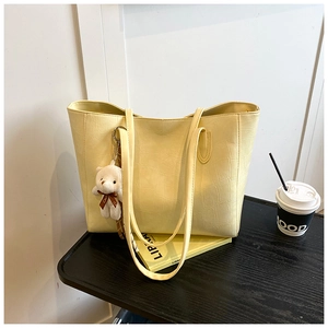 Close-up of yellow crocodile embossed tote bag with a cute plush bear charm detail
