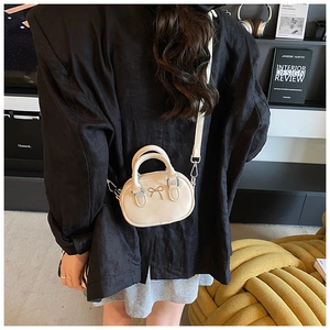 Mini cream bowling bag with metal bow detail shown on black blazer for lifestyle look