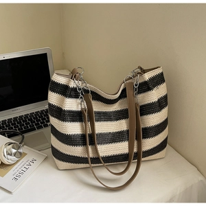 Detail of a black and white striped woven tote bag with brown leather straps and silver chains
