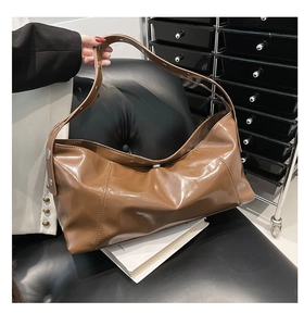 Detail of glossy brown oil wax leather shoulder bag with silver studded strap on a black chair