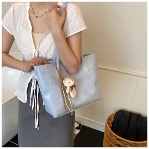 Détail d'un sac cabas bleu clair à texture crocodile avec breloque ours sur modèle