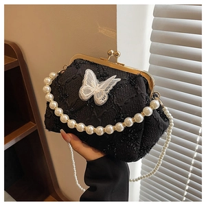 Detail of black pleated kiss-lock bag featuring a lace butterfly and pearl handles