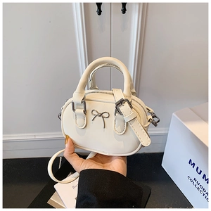Close-up of a mini cream bowling bag with a silver bow detail and detachable strap