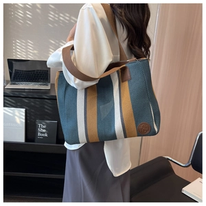 Detail of large woven canvas tote bag with blue and brown vertical stripes and leather strap