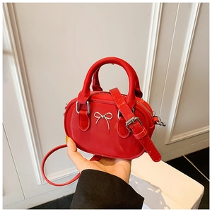 Close-up of red mini bowling bag with bow detail held by hand to show compact size