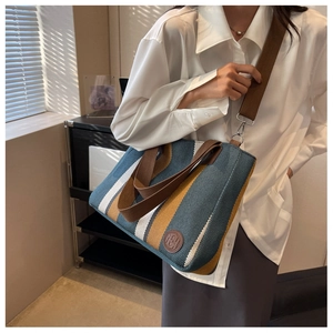 Close-up of a striped canvas tote bag with brown leather logo and adjustable strap