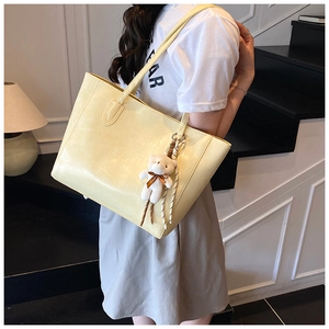 Detail of pale yellow crocodile embossed tote bag featuring a cute white plush bear pendant