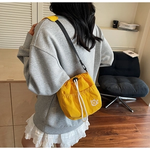 Model wearing a yellow nylon bucket bag with drawstring closure in a cozy home setting