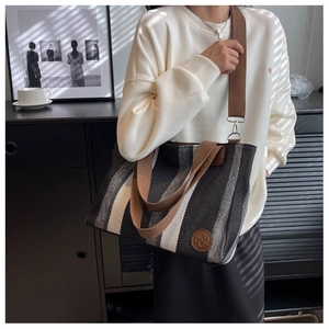 Close-up of vertical striped canvas tote bag with brown woven strap and leather logo