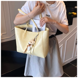 Detail of light yellow tote bag with crocodile pattern and cute bear charm decoration