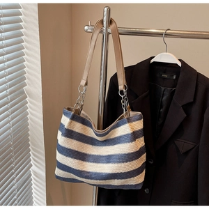Close-up of woven blue and white striped tote bag with brown leather straps and chains