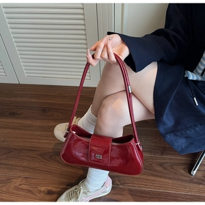 Détail du sac baguette en cuir verni rouge avec logo en métal argenté et bandoulière fine