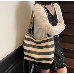 Detail of woven striped tote bag featuring brown leather shoulder strap and metallic chain links