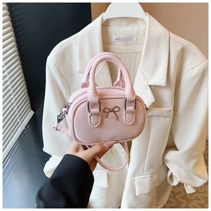 Mini pink bowling bag with silver bow detail held against a beige blazer outfit