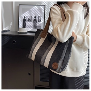 Detail of large canvas tote bag with vertical stripes and premium brown leather handles