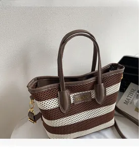 Detail der gestreiften Stricktasche mit braunen Ledergriffen und goldenen Metallteilen