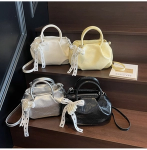 Detail view of four pleated mini tote bags in black, silver, white and yellow with pearl bows