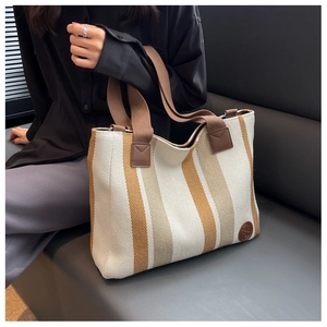 Close-up of a striped canvas tote bag with brown handles and a leather logo on a sofa