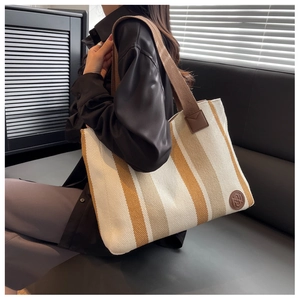 Detail of striped canvas tote bag with brown leather logo and reinforced shoulder strap