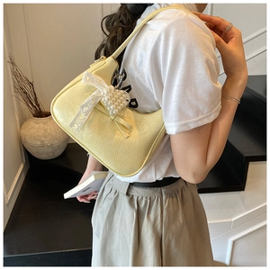 Detail der gelben Hobo-Tasche mit weißer Spitzenschleife und Perlenherz am Modell
