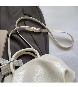Detail of white pleated bucket bag with shiny texture and elegant pearl lace charm