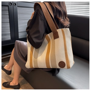 Detail of knit striped tote bag with wide shoulder strap on a black leather sofa
